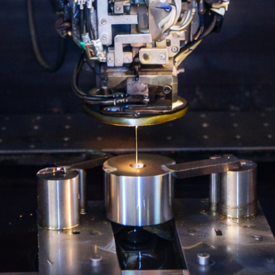 Bild: Das Bild zeigt eine Maschine zur Drahterosion, die gerade ein Metallstück bearbeitet, Die Mitte des Metallstücks glüht.